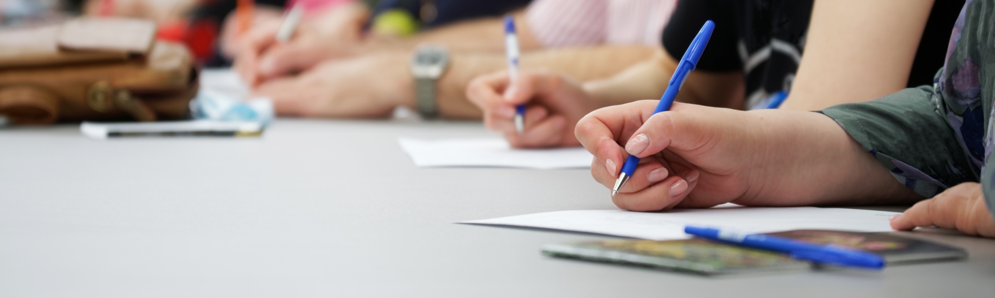 High school students' hands poised to write on paper a response to a listening comprehension task