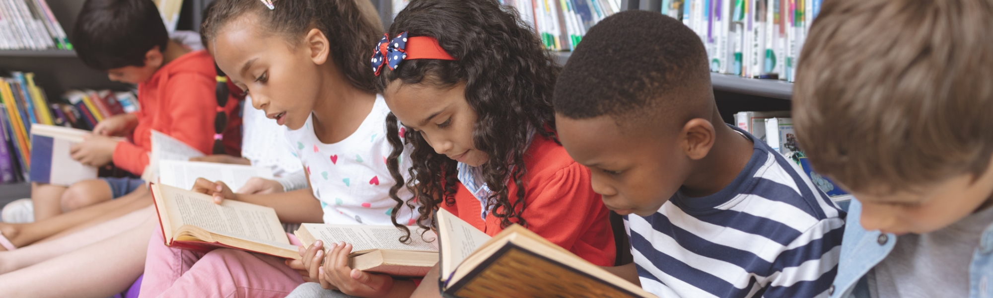 Elementary school children reading books in front of bookshelves in a library